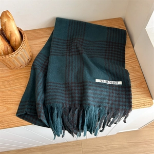 Detail of soft plaid scarf with tassels and brand label on a wooden surface