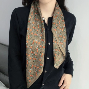Detail of floral print scarf in tan and orange wool blend on a model in home setting