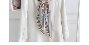 Détail d'un foulard en soie à motif chaîne stylisé sur un blazer blanc à double boutonnage