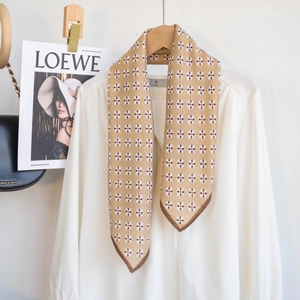 Detail eines beigen Halstuchs mit braunem Blumenmuster an einer weißen Chiffonbluse