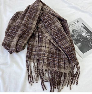 Close-up of thick knit brown plaid scarf with fringe tassels on white textured background