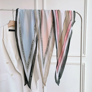 Silk neck scarves with geometric V-pattern and French text hanging on a white rack