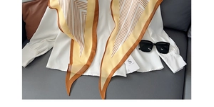 Detail van een geel gestreepte zijden sjaal op wit shirt met een zonnebril