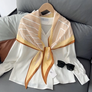 Elegante witte blouse met geel gestreepte zijden sjaal op een houten kledinghanger