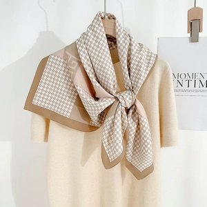 Detail view of square silk scarf with houndstooth and geometric patterns on a beige sweater