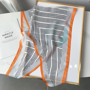 Detailweergave van een lichte zijden sjaal met blauwe stippen en oranje gestikte randen