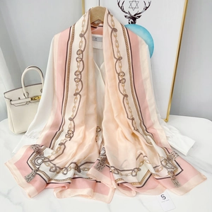 Elegant long silk scarf with pink and cream chain print draped over a white blouse