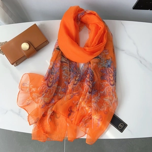 Detail view of bright orange lightweight shawl with colorful paisley floral pattern on marble