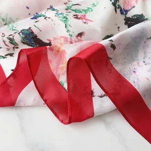 Macro detail of silk-like scarf with floral print and bold red border on marble