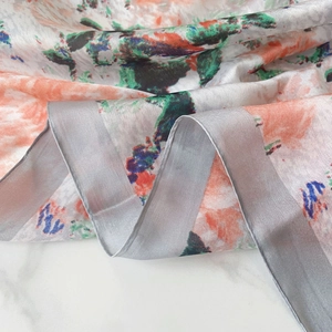 Close-up of silk scarf fabric showing abstract floral pattern and rolled hem detail