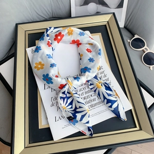 Detail of floral silk scarf with daisies next to sunglasses and a gold frame