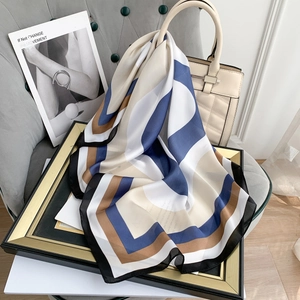 Detail of a geometric silk-like scarf styled as a decorative accessory on a beige handbag