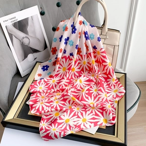 Detail of colorful daisy printed silk scarf draped over a white leather handbag on a chair