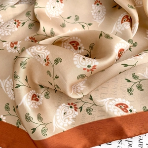 Detailed macro view of champagne silk scarf with paisley floral pattern and orange border
