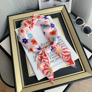 Close-up of pink satin scarf with colorful daisies on a golden tray with a magazine