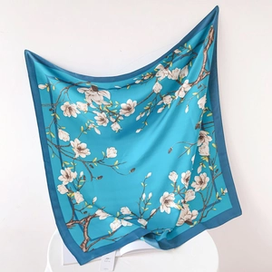 Detail of elegant silk-like square scarf with white magnolia print on turquoise background