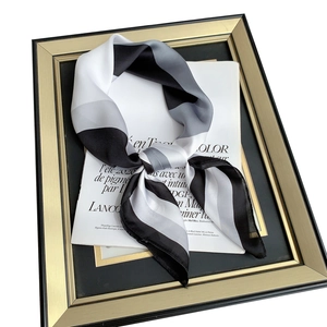 Elegant silk-like square scarf with black, white, and grey geometric patterns on a satin surface