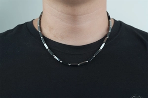 Detail of a dark gray beaded titanium steel necklace on a male model wearing a black tee