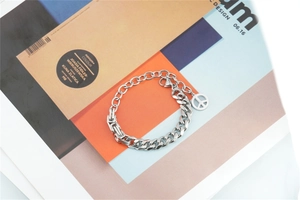Detail of silver Cuban chain bracelet featuring a peace sign pendant on magazine background