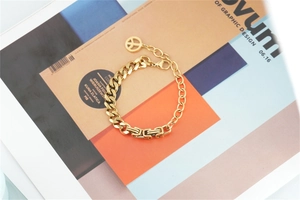 Detail of a gold-plated Cuban link bracelet with a peace sign pendant on a fashion magazine