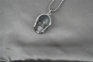 Vue détaillée du dos texturé d'un pendentif tête de mort gothique sur du satin gris