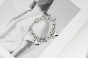 Close-up of double-layer silver chain bracelet with heart and sphere charms on a magazine