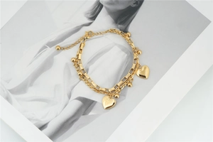 Detail of a gold double-layer chain bracelet featuring heart pendants and a lobster clasp