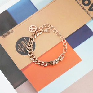 Rose gold Cuban link bracelet with peace sign charm on a minimalist jewelry magazine background