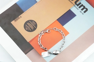 Detail of silver stainless steel chain bracelet with square Good Luck charm and oval bead