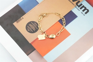 Detail of gold chain bracelet with Good Luck tag and oval bead on art magazine