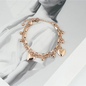 Rose gold double-layer chain bracelet featuring heart charms and beads on magazine background
