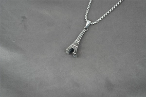 Detail of silver Eiffel Tower pendant on box chain over grey textured background