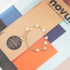 Bracelet en acier titane doré avec perles blanches et boules de strass sur fond magazine