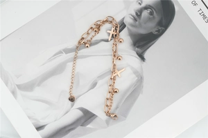 Detail view of a rose gold layered bracelet with cross and ball charms on a magazine base