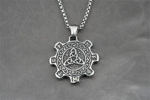 Macro shot of silver gear pendant with Celtic knots and Rune symbols on grey fabric