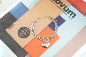 Asymmetric silver chain bracelet featuring a polished heart pendant on art magazine