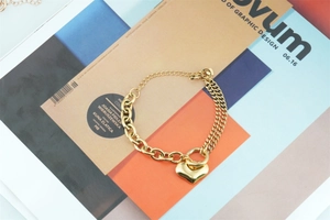 Detail of a gold-toned double chain bracelet with a heart pendant and toggle clasp