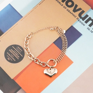 Golden asymmetrical double chain bracelet with a polished 3D heart charm on a magazine