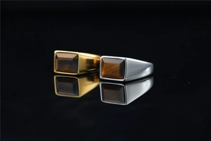 Macro shot of silver and gold men's rings with rectangular tiger eye stones on black mirror
