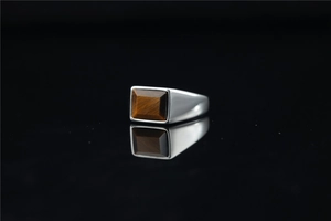 Macro detail of men's square-cut tiger eye stone ring on a polished black reflective surface