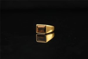 Detailed view of men's gold ring with rectangular tiger eye stone on reflective black surface