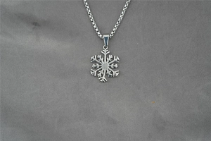Détail du pendentif flocon de neige ajouré avec chaîne vénitienne sur tissu gris