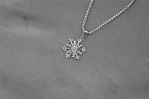 Gros plan du pendentif flocon de neige avec chaîne en acier sur tissu gris