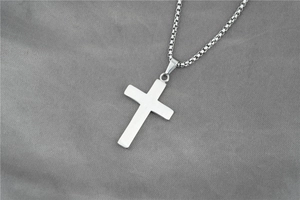 Vue détaillée du pendentif croix argenté avec chaîne gourmette polie sur tissu gris