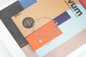 Detail of a double-layered titanium steel bracelet with a heart pendant and bead chain
