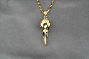 Macro detail of golden crow skull pendant with black textured accents on a box chain