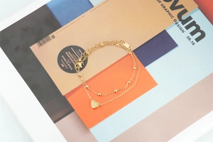 Detail of a layered golden titanium steel bracelet featuring a polished heart charm