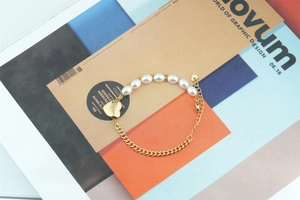 Détail du bracelet gourmette doré avec perles blanches et un pendentif en cœur