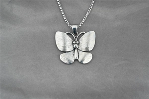 Detail of butterfly pendant with brushed metal texture on a square box chain