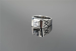 Macro shot of a wide stainless steel ring with a center diamond and engraved geometric motifs